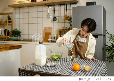 Young man pouring cereal into bowl for breakfast at home kitchen table 126198975