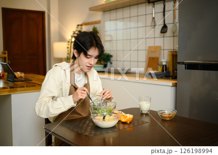 Young Asian man eating healthy breakfast with salad and milk in a kitchen Young Asian man eating healthy breakfast with salad and milk in a kitchen 126198994