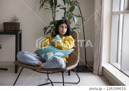 Sad unhappy young beautiful lady sitting in armchair hugging pillow Sad unhappy young beautiful lady sitting in armchair hugging pillow 126199018