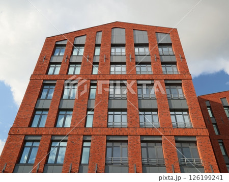 A modern red brick building stands tall under a blue sky, showcasing vibrant design elements A modern red brick building stands tall under a blue sky, showcasing vibrant design elements 126199241