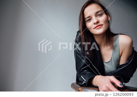 Portrait of a beautiful brunette woman in a leather jacket on a gray background 126200093
