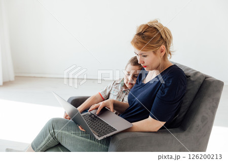 Mom And Son Sitting In Chair With Laptop Online In Room 126200213