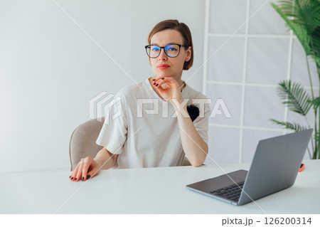 woman in glasses working at desk with laptop in office online 126200314
