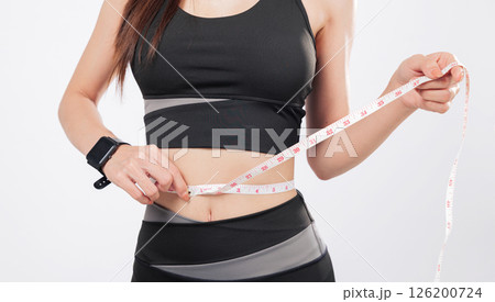 Tape for tracking and tape for success, this smiling woman in sport attire proudly measures her slim waist, celebrating weight loss and healthy living. isolated studio white background Tape for tracking and tape for success, this smiling woman in sport attire proudly measures her slim waist, celebrating weight loss and healthy living. isolated studio white background 126200724