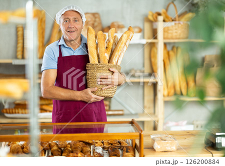 Bakery senior man employee holds basket of ready-made baguettes 126200884
