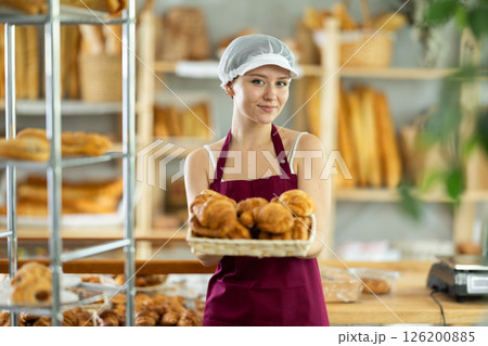 Bakery young woman employee holds basket of ready-made croissant 126200885