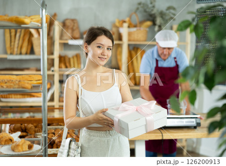 Cute young girl customer holding box with decorative bow and buying sweet authors flour products in bakery shop 126200913