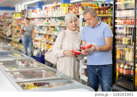 Senior couple looking at goods in glass showcase in supermarket Senior couple looking at goods in glass showcase in supermarket 126201091