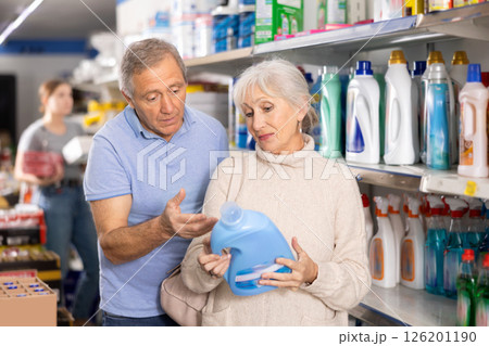 MAture couple shopping in supermarket, chooses plastic bottle of household detergent MAture couple shopping in supermarket, chooses plastic bottle of household detergent 126201190