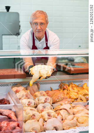 Senior man butcher shop owner offering raw chickens 126201192