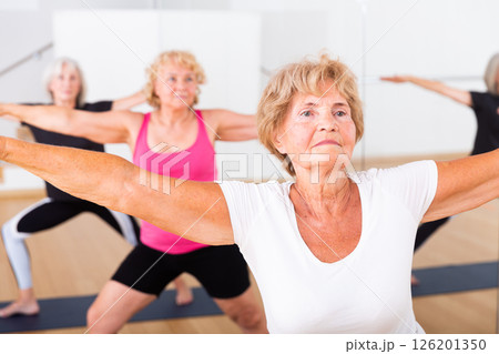 Three mature women perform the exercise by taking the warrior pose II 126201350