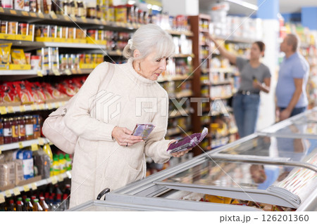 Old woman purchaser choosing frozen product in big supermarket 126201360