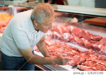 Male pensioner customer points with finger and orders beef brisket and sirloin 126201390