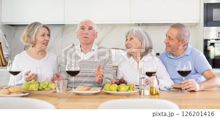 Two mature married couples are sitting at table, enjoying food and wine, chatting. 126201416