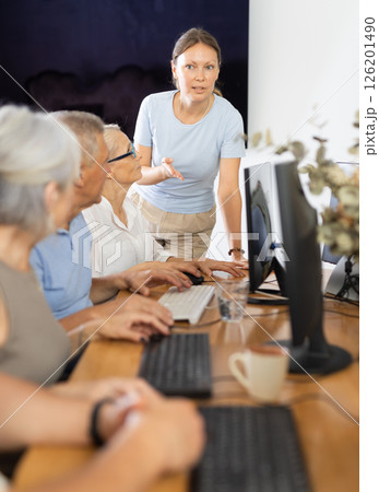 Mature people listen attentively to female teacher during computer teaching lesson in nursing home 126201490