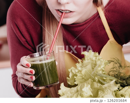 Woman in kitchen holding vegetable smoothie juice Woman in kitchen holding vegetable smoothie juice 126201684