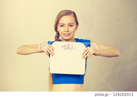 Teenage woman holding bathroom scale machine Teenage woman holding bathroom scale machine 126202011
