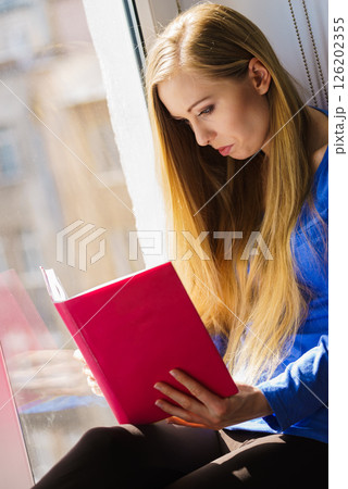 Woman sitting on window sill reading book at home 126202355