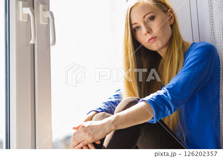 Sad depressed teen girl sitting on window sill Sad depressed teen girl sitting on window sill 126202357