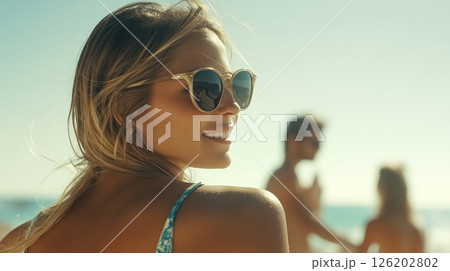 Woman enjoys a sunny day at the beach with sunglasses, smiling enigmatically while turning her head left 126202802