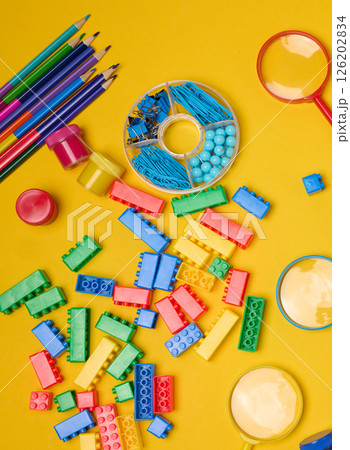 Vibrant collection of colorful school supplies, building bricks, letters, and learning items scattered on a yellow background. Play and education concept. 126202834