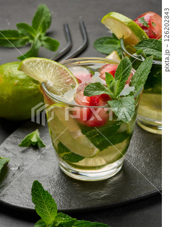 Refreshing mojito cocktail with lime, mint, strawberry, and ice on dark background Refreshing mojito cocktail with lime, mint, strawberry, and ice on dark background 126202843