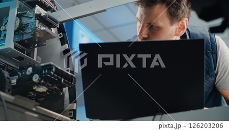 Technician in Uniform Using Laptop, Adjusting Internal Components of ATM Machine Technician in Uniform Using Laptop, Adjusting Internal Components of ATM Machine 126203206