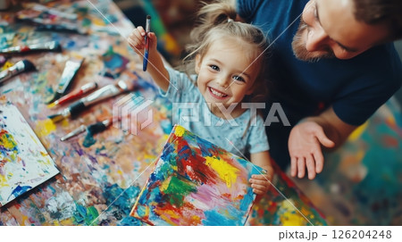 Little girl proudly shows her colorful painting to her dad during a joyful art session 126204248