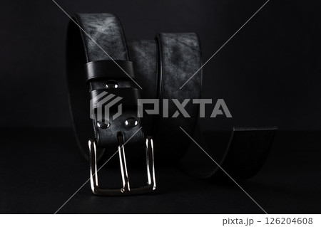 A black belt with a silver buckle is laying on a black surface. The belt is made of leather and has a silver buckle A black belt with a silver buckle is laying on a black surface. The belt is made of leather and has a silver buckle 126204608