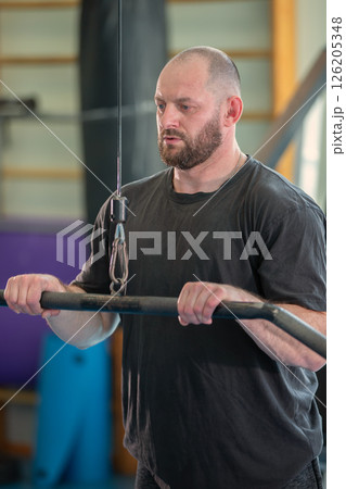 A man is lifting weights in a gym. He is wearing a black shirt and has a beard A man is lifting weights in a gym. He is wearing a black shirt and has a beard 126205348
