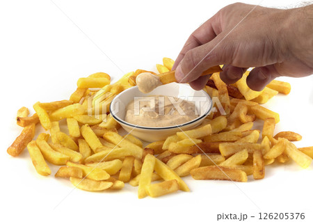 A hand dips French fries into a white bowl of sauce. A hand dips French fries into a white bowl of sauce. 126205376