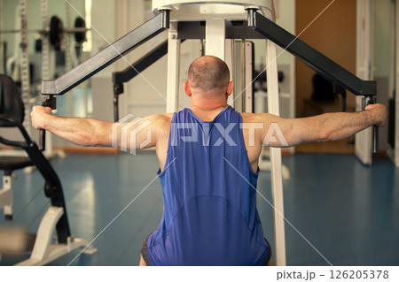 Male athlete exercises on a strength training machine in a gym. Back view. 126205378