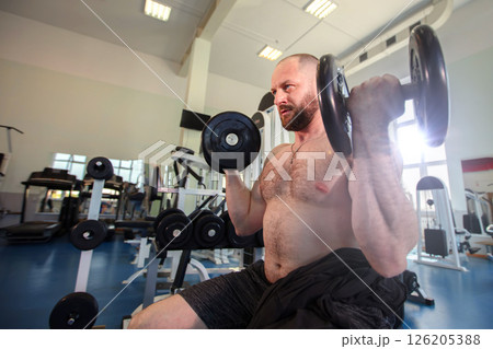A man lifts weights in a gym equipped with various machines and weights A man lifts weights in a gym equipped with various machines and weights 126205388