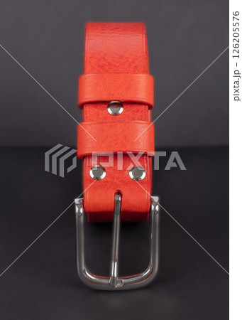 Red leather belt with metal buckles on a gray background. 126205576