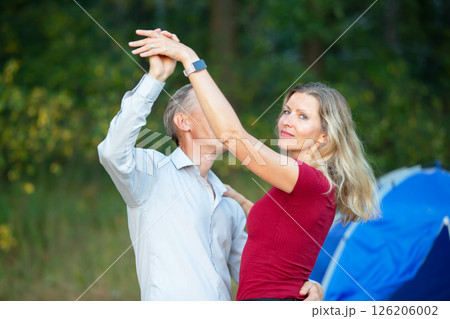A beautiful adult woman is dancing with a man. She is looking at the camera and his face is covered with his hand. A beautiful adult woman is dancing with a man. She is looking at the camera and his face is covered with his hand. 126206002