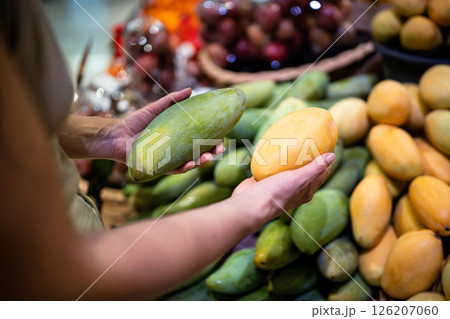 Woman hand selecting ripe mango fruit from variety on market counter for healthy diet choice Woman hand selecting ripe mango fruit from variety on market counter for healthy diet choice 126207060