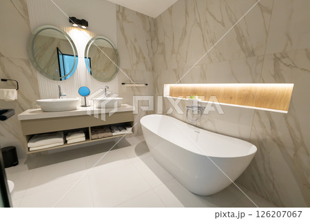A modern elegant hotel bathroom with freestanding bathtub, double sink and round mirrors 126207067