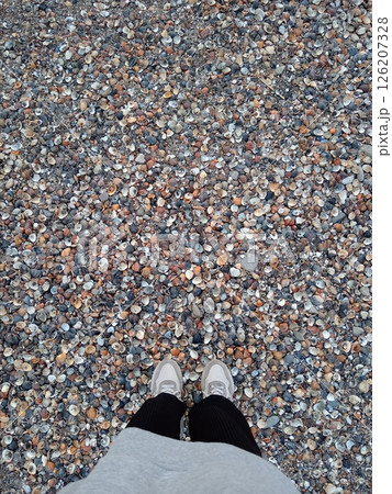 shell beach of the Caspian Sea, Makhachkala, Russia, legs of a girl in light sneakers, top view 126207328