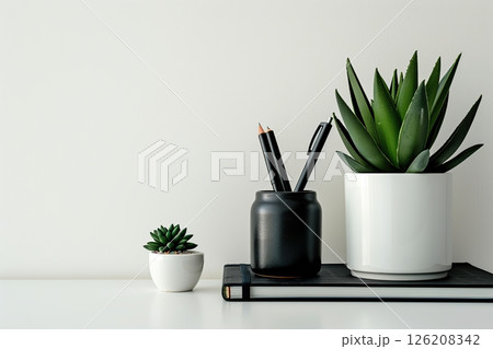 Front view white desk with black stationery, succulent plant, notebook, eyeglasses. Morning background banner, space for text. Minimalistic concept, workspace, time to work. Blank workplace. Mock-up. 126208342