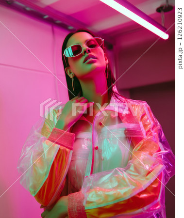 Fashion y2k model posing in translucent jacket with neon pink sunglasses in studio light 126210923