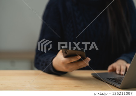 Person using smartphone and laptop on wooden table with cozy atmosphere for remote work or digital communication concept 126211097