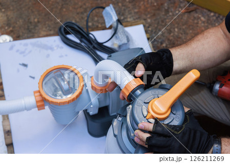 Individual is connecting parts of water pump to pool filter in outdoor setting Individual is connecting parts of water pump to pool filter in outdoor setting 126211269