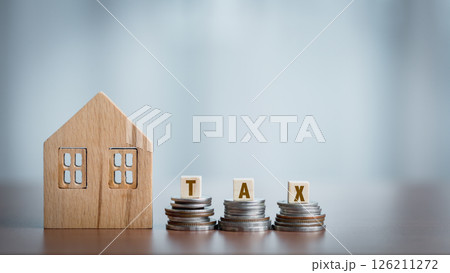 Wooden house model and coin stack with TAX word on wooden table. 126211272