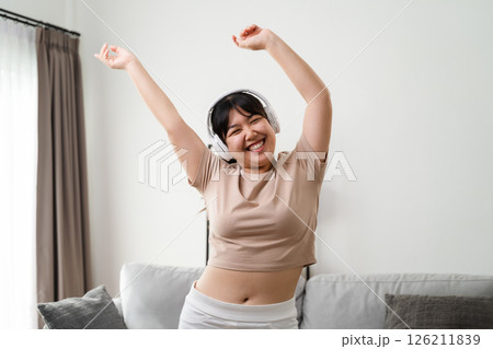 Asian woman listening to music happily, having fun and relaxing with headphones in living room. 126211839