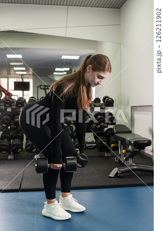 Young woman doing dumbbell deadlift in fitness studio. 126211902