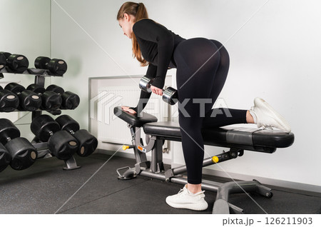 Woman doing dumbbell row on bench in modern gym. 126211903