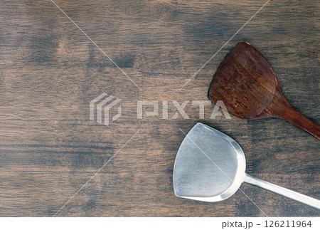 Wooden and metal spatulas on rustic wooden table, showcasing blend of natural and industrial materials. contrast highlights versatility and functionality of kitchen tools 126211964