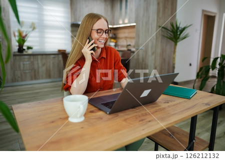 Cheerful woman working from home while talking on the phone Cheerful woman working from home while talking on the phone 126212132