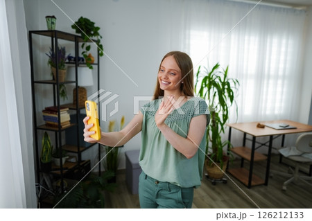 Smiling woman waving at friends during a virtual call at home 126212133