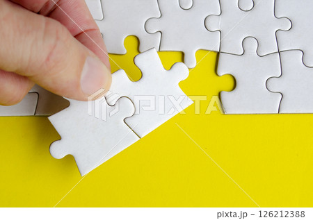 Hand holding jigsaw puzzle pieces on a bright yellow background with customizable space on jigsaw for text or ideas. Hand holding jigsaw puzzle pieces on a bright yellow background with customizable space on jigsaw for text or ideas. 126212388